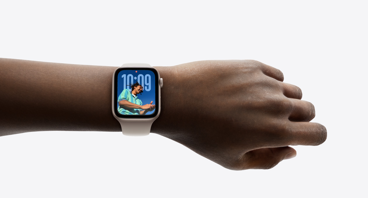 Gros plan d’une Apple Watch or rose avec un bracelet en caoutchouc au poignet d’une personne, qui affiche l’heure avec le nouveau design Liquid Glass