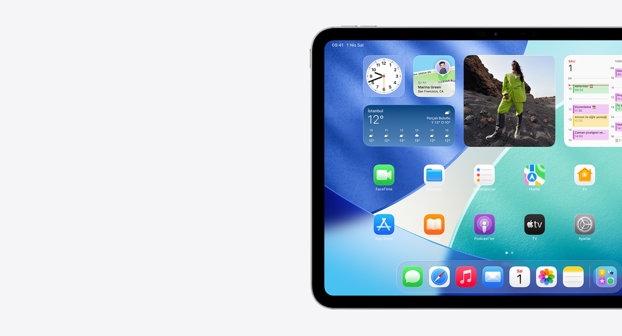 iPad, yatay pozisyonda, ekranın yalnızca sol tarafı görülüyor, Ana Ekran’da Liquid Glass efekti gösteren yarı saydam saat, Bul uygulaması ve Hava Durumu araç takımıları, iki sıra halinde daha küçük uygulamalar ve Dock yer alıyor