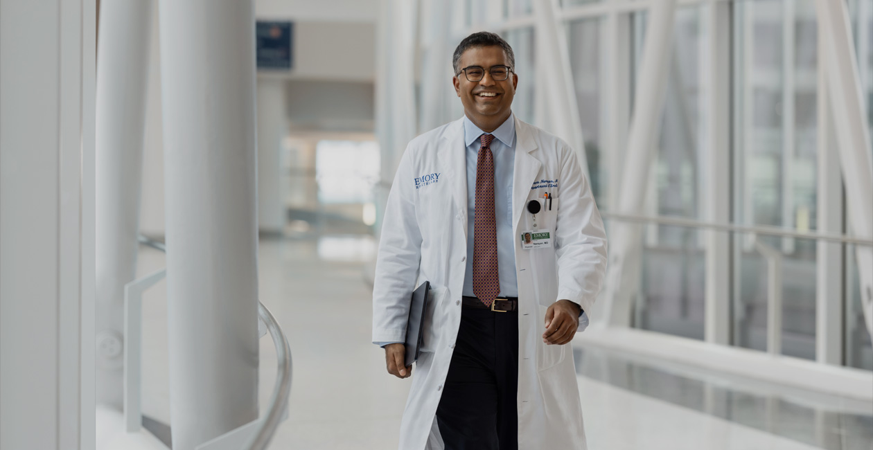 Un médecin qui marche en tenant un MacBook sous son bras droit.