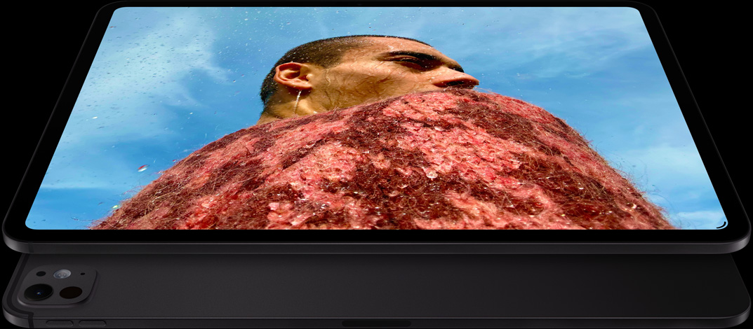 iPad Pro i space black vist skråt forfra i vandret position, afrundede hjørner, sort skærmkant, skærmen viser et billede af en mand i en rød striktrøje under en blå himmel, nedenunder vises en anden iPad Pro i space black skråt bagfra i vandret position med Pro-kamerasystem og lydstyrkeknapper